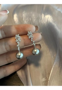 Macro shot of silver pearl earrings with zircon embellishments on purple silk