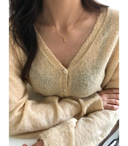 Gros plan du collier pendentif fleur croisée dorée porté avec un cardigan en mohair beige