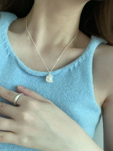 Close-up of s925 silver flower necklace with pearl pendant worn with a blue knit vest