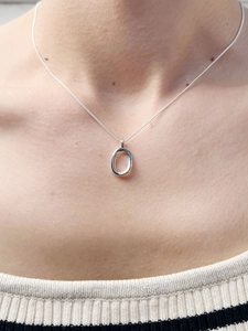 Close-up of minimalist 925 silver necklace with oval pendant worn on the collarbone