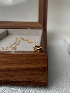 Détail d'un pendentif tonneau doré avec trois pierres étincelantes sur un écrin à bijoux en bois