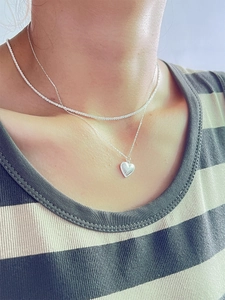 Detail of double-layer silver heart necklace with sunburst engraving on female model