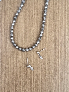 Macro detail of S925 silver leaf earrings and beaded necklace on a wooden background