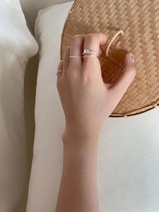 Detail of silver wavy ring set and knotted design worn on fingers over a bamboo surface