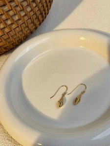 Close-up of gold conch shell drop earrings on a white ceramic plate with warm lighting