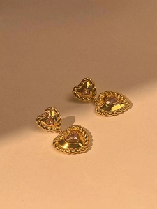 Détail de boucles d'oreilles cœur en argent doré avec zircon rose et bordure tressée