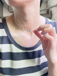Détail du collier en argent S925 plaqué or avec pendentifs en émail noir porté par un modèle
