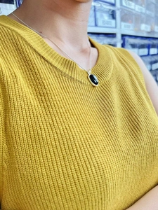 Detail of an oval black agate pendant on a silver chain worn with a yellow vest