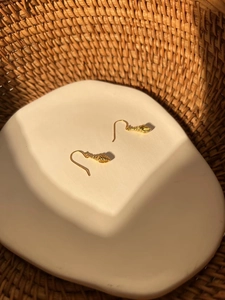 Macro shot of gold seashell drop earrings with spiral texture on a white ceramic plate