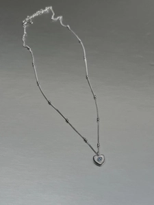 Detailed shot of 925 silver heart necklace with blue gem and beaded chain on grey surface