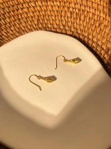Detailed close-up of golden conch shell dangle earrings on a textured ceramic dish