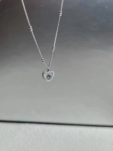 Macro detail of silver heart pendant with textured radial pattern and blue sapphire gem