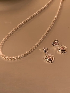 Détail des boucles d'oreilles torsadées dorées avec pierres cœur roses et collier de perles
