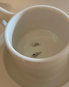 Macro shot of silver conch shell hook earrings resting inside a white ceramic cup