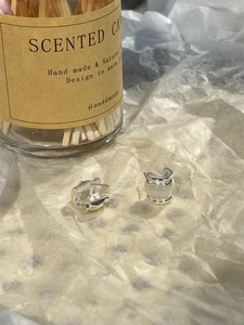 Close-up of polished silver C-shaped earrings on a beige textured background
