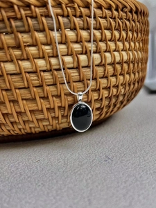 Minimalist 925 silver necklace with black agate oval pendant on a woven basket