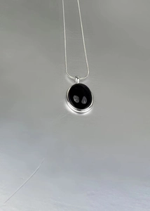 Detailed view of oval black onyx pendant on polished silver snake chain necklace