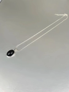 Macro detail of 925 silver snake chain with an oval black onyx pendant on grey surface