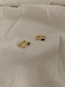 Macro detail of gold textured square earrings with black onyx and zircon on linen cloth