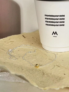 Minimalist 925 sterling silver ball necklace with golden polished bead pendant on beige surface