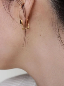 Close-up of a gold U-shaped earring with irregular texture worn by a model