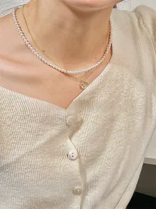 Détail d'un collier doré multicouche avec perles et pendentif rose sur un mannequin