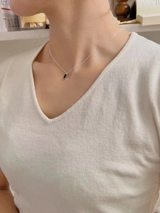 Gros plan d'un collier argenté avec pendentif rectangle noir porté par un mannequin
