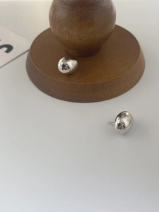 Detail of high-polished 925 sterling silver bean earrings on a minimalist wooden stand