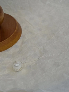 Macro shot of a round white pearl pendant with a textured silver setting and chain