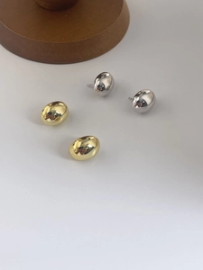 Close-up of gold and silver bean stud earrings with a polished mirror finish on a minimalist base