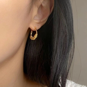 Gros plan d'une boucle d'oreille créole torsadée dorée portée par un mannequin chic