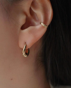 Gros plan d'une boucle d'oreille goutte dorée et d'un ear cuff tissé sur une oreille