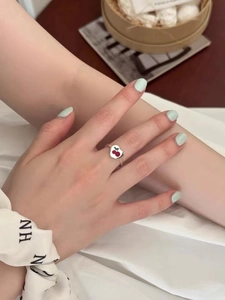 Cute silver open ring with red cherry heart design on model hand with soft lighting