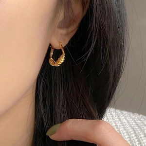 Gros plan sur une boucle d'oreille créole torsadée dorée portée par un mannequin en détail
