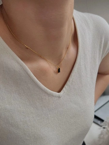 Collier doré avec pendentif rectangulaire en pierre noire porté sur un pull blanc en V