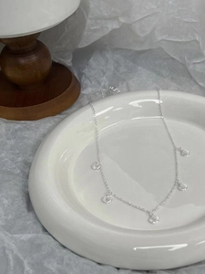 Macro detail of S925 silver choker with five delicate shell charms on a white ceramic plate