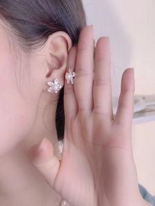 Macro shot of 925 silver petal earrings with white pearl centers on model's ear
