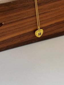 Detail einer goldenen Herzenskette mit graviertem H-Buchstaben und gedrehter Seilkante