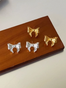 Macro view of textured metal bow earrings in gold and silver finish on a wooden stand