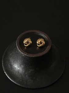 Macro detail of polished gold multi-strand knot stud earrings on black ceramic stand