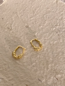 Détail de boucles d'oreilles créoles dorées torsadées au design minimaliste chic