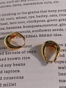 Vue détaillée des boucles d'oreilles créoles dorées en U sur fond de livre ouvert