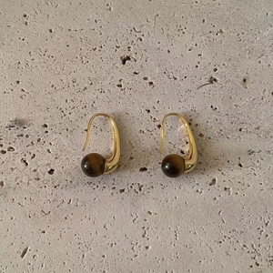 Elegant gold drop earrings with polished brown tiger eye stone beads on stone background