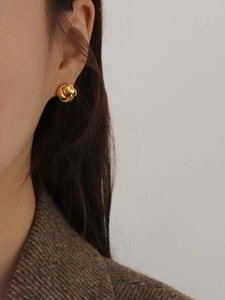 Close-up of elegant gold knot stud earrings worn by a model with tweed texture
