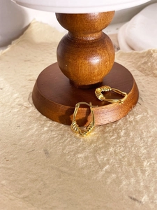 Détail de boucles d'oreilles créoles dorées avec texture filaire sur socle en bois
