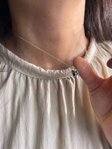 Close-up of minimalist sterling silver heart necklace with black stone on a model