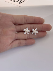 Macro shot of 925 silver pearl flower earrings with micro-set zircons on hand
