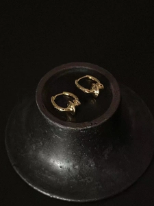 Macro detail of gold-plated hoop earrings with delicate bow design on dark surface