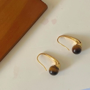 Detail of golden hook earrings featuring polished round tiger eye stone beads