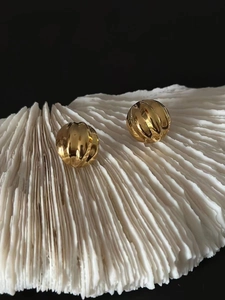 Macro shot of gold sphere earrings with spiral textures on white coral background